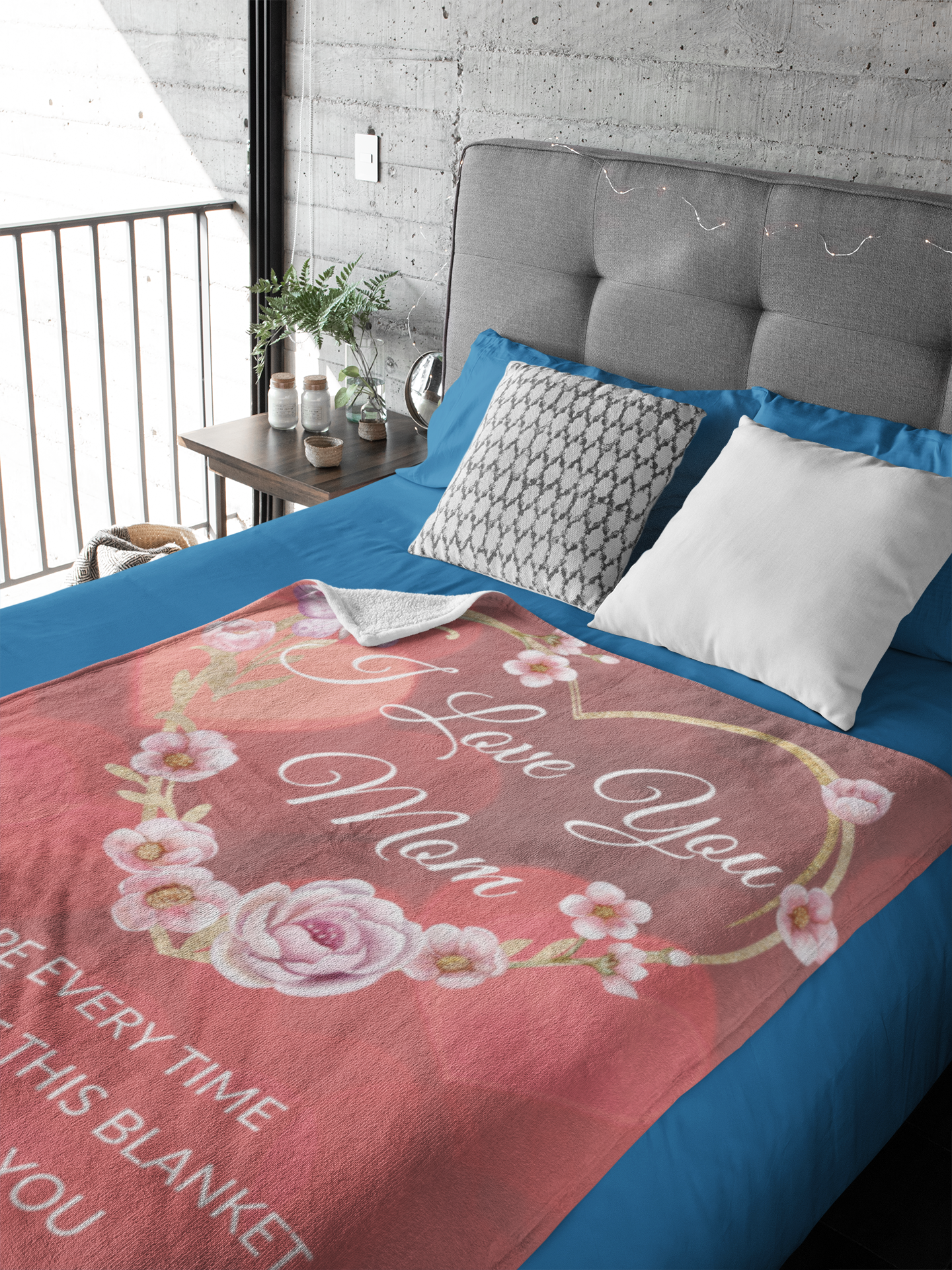 A premium Sherpa blanket with a design of a flower-covered golden heart and the message 'I love you mom'. The blanket offers ultimate comfort with a silky smooth front, fluffy sherpa back, a luxurious thickness of 1 cm. draped over a bed